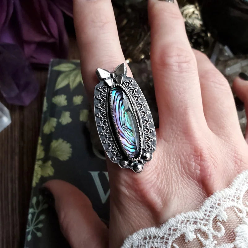 a woman’s hand holding a ring with a rainbow colored stone