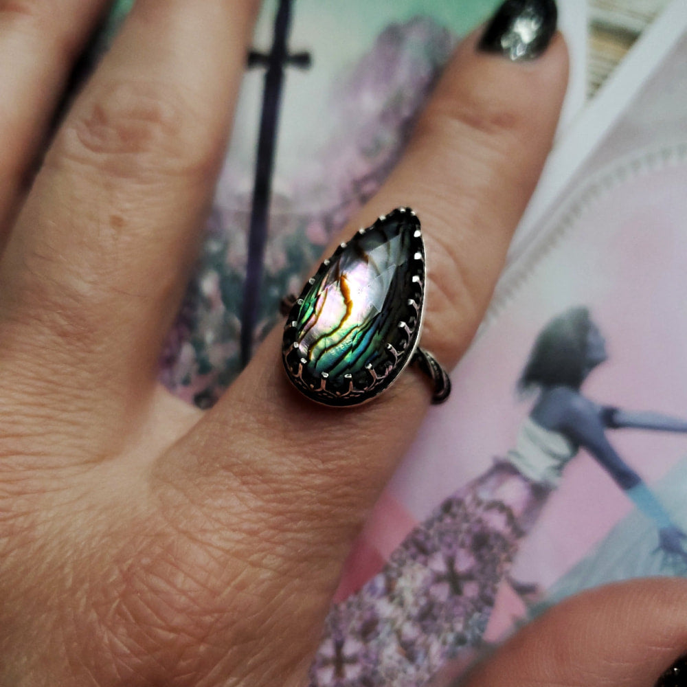 a woman’s hand holding a ring with a rainbow colored stone