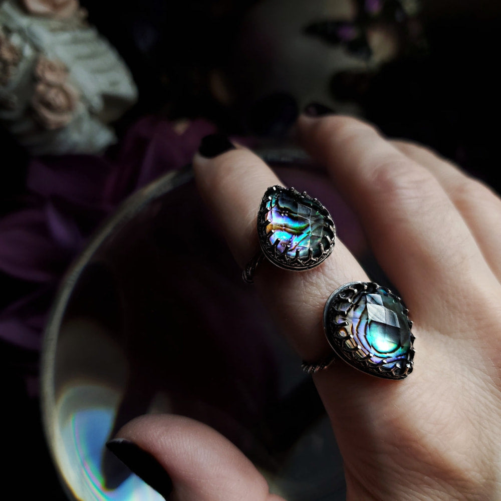 a woman’s hand holding a ring with a rainbow colored stone