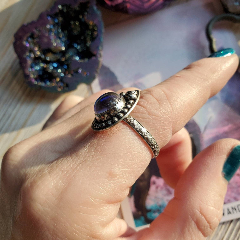 a woman’s hand holding a ring with a large purple stone