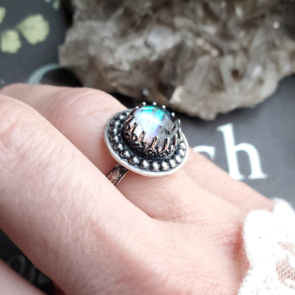 a person holding a ring with a rainbow colored stone