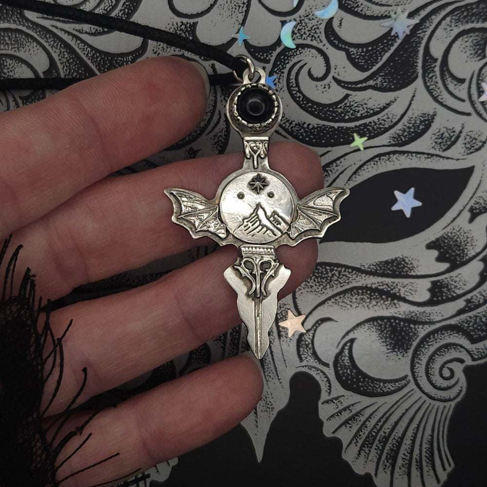 Silver-colored pendant with bat wings and mountain scene.