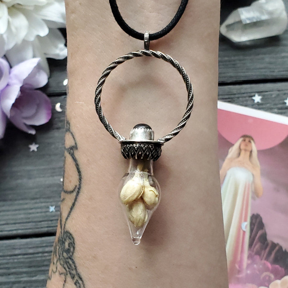a woman’s hand holding a silver pendant with a white flower