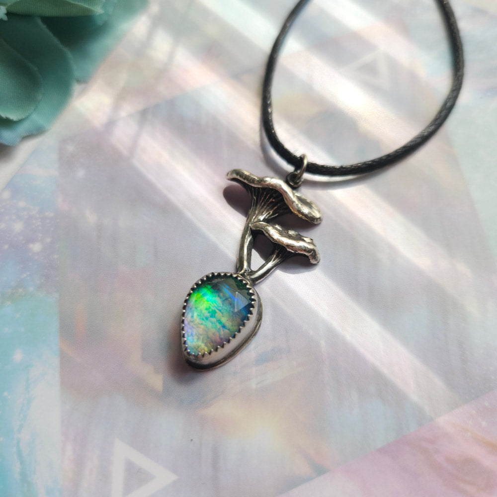 Mushroom-shaped pendant with an iridescent opal gemstone hanging from a black cord necklace.
