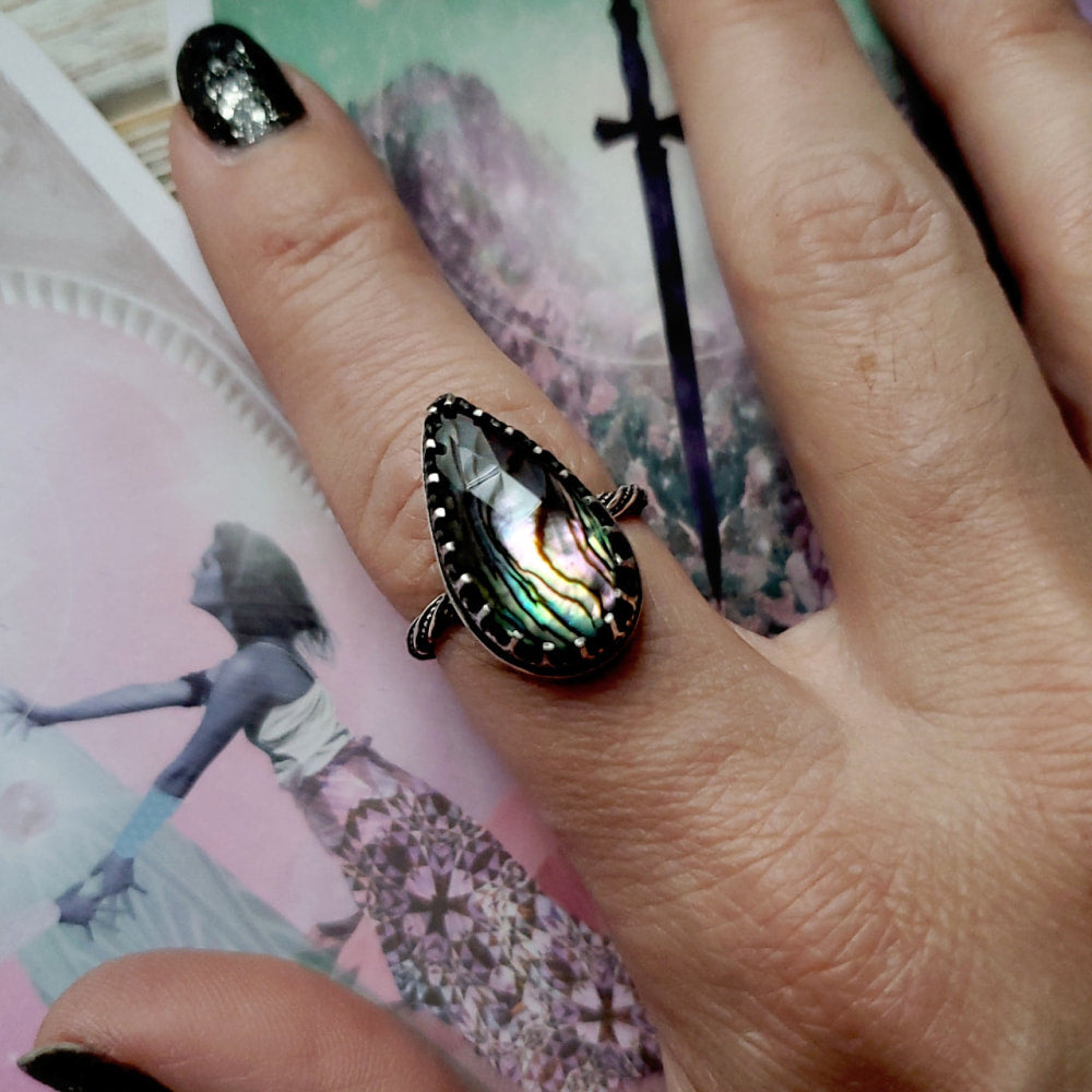 a woman’s hand holding a ring with a rainbow colored stone