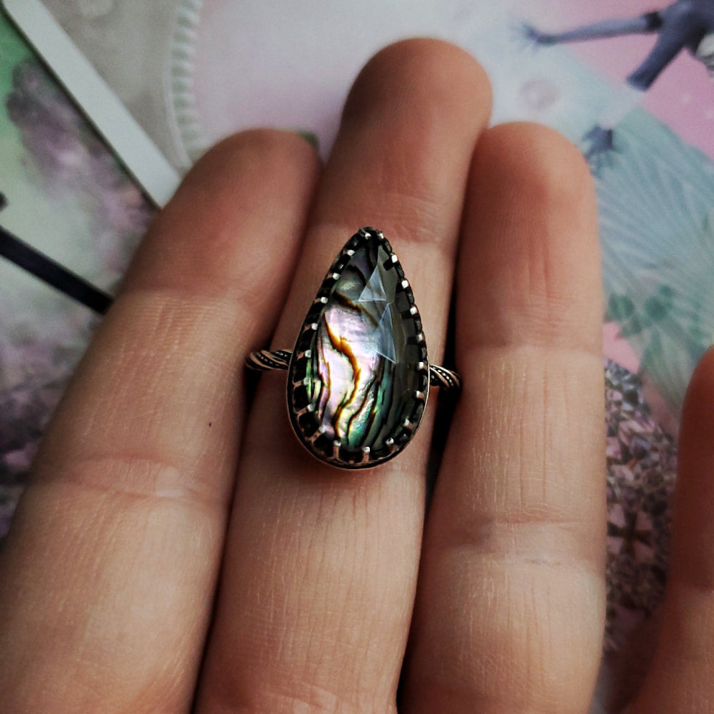 a woman’s hand holding a ring with a large black and white stone