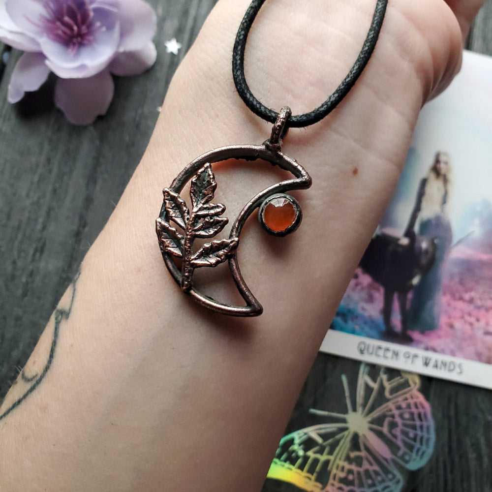 a woman’s hand holding a copper pendant with a crescent and a crescent