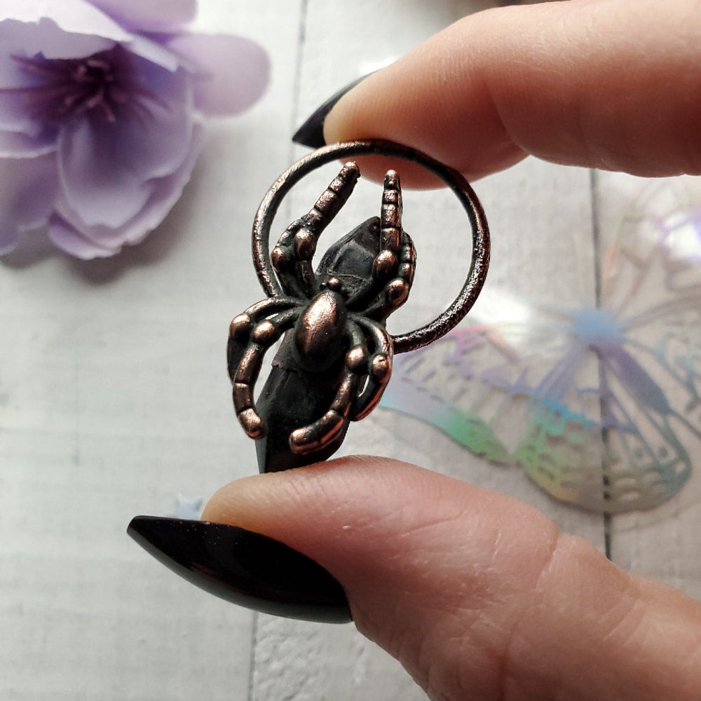 Metal spider pendant or charm held between fingertips.