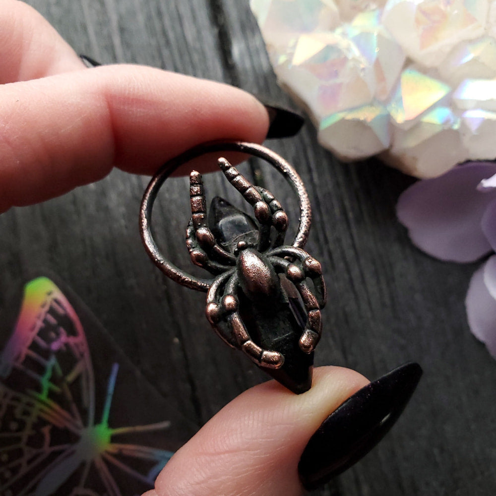 Metal spider-shaped pendant or charm held between fingers.